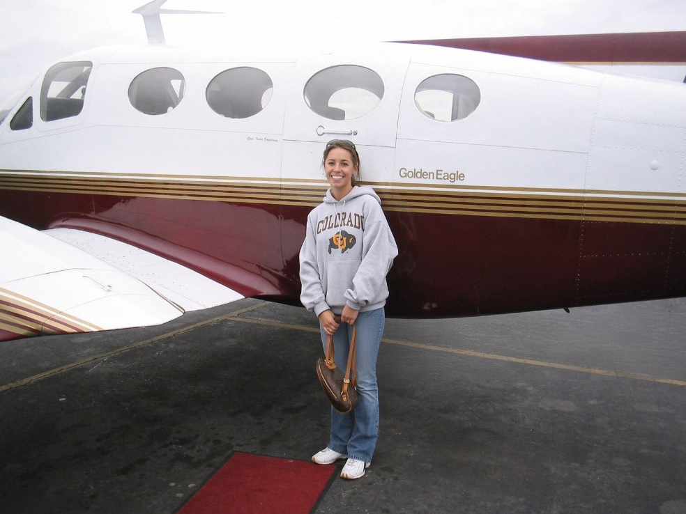 Nadia Barghelame smiling on the tarmac in front of her Golden Eagle airplane, wearing a Colorado hoodie